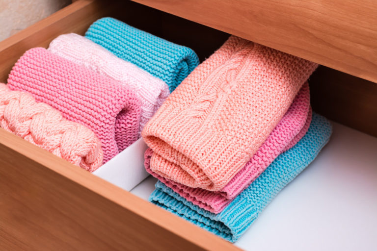 Organization and order. A stack of knitted clothes next to a box of neatly folded items in a dresser drawer