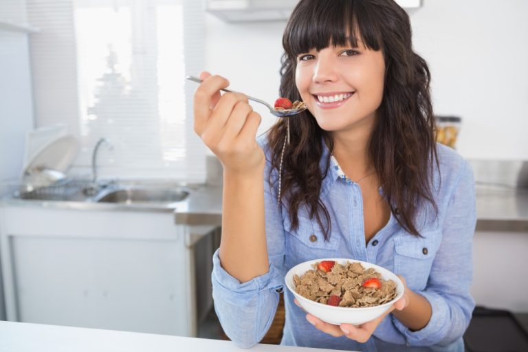 A woman enjoying while eating her cereal and fruits in a bowl