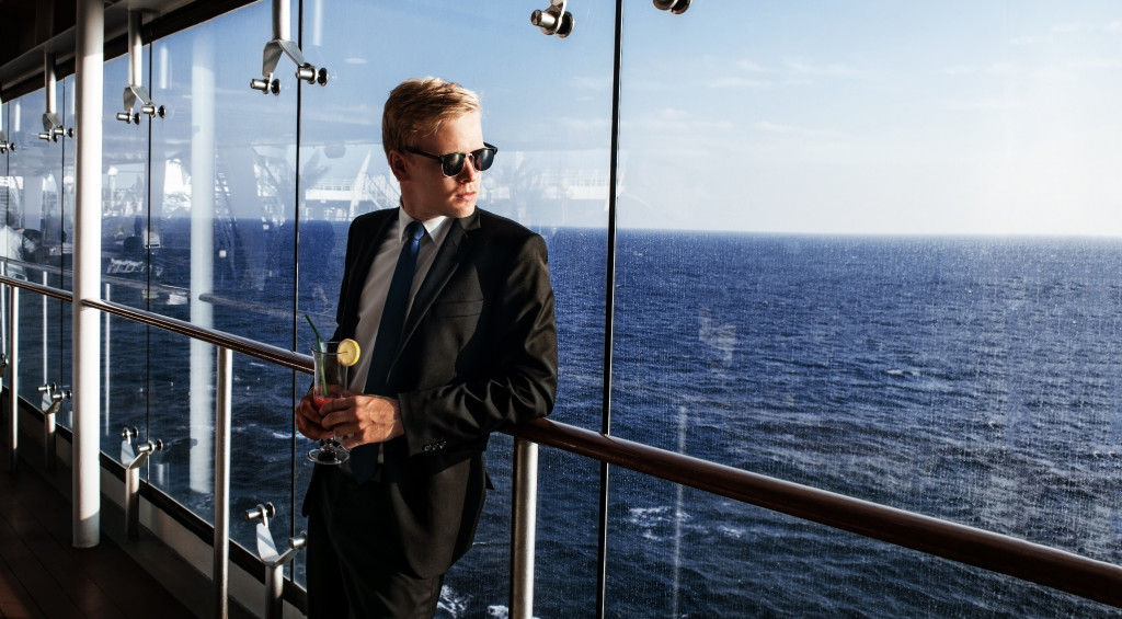 a wealthy man in sunglasses leaning over a cruise railing