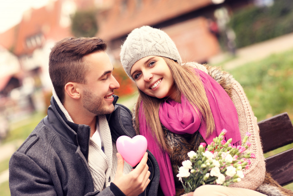 Smiling young couple on a date in the park with a heart and flowers.